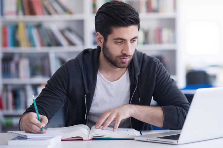 A photo of a man writing and using a laptop