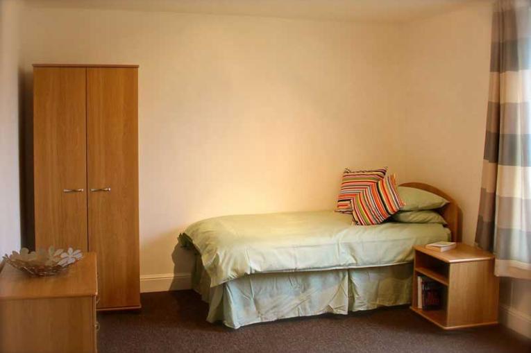A bedroom with a single bed, a single wardrobe, bedside table and checked curtains
