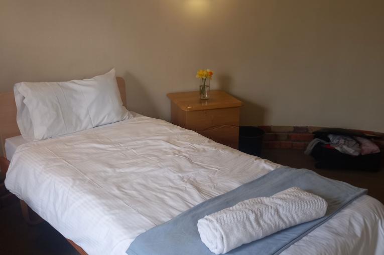 Bridge House Bedroom - a white single bed in a room with white walls. Towels are laid out on the bed