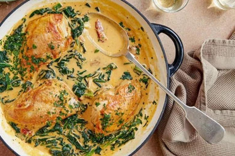 A photo of a ceramic cooking pot with chicken breasts in a yellow, creamy sauce and green herbs sprinkled on top. 