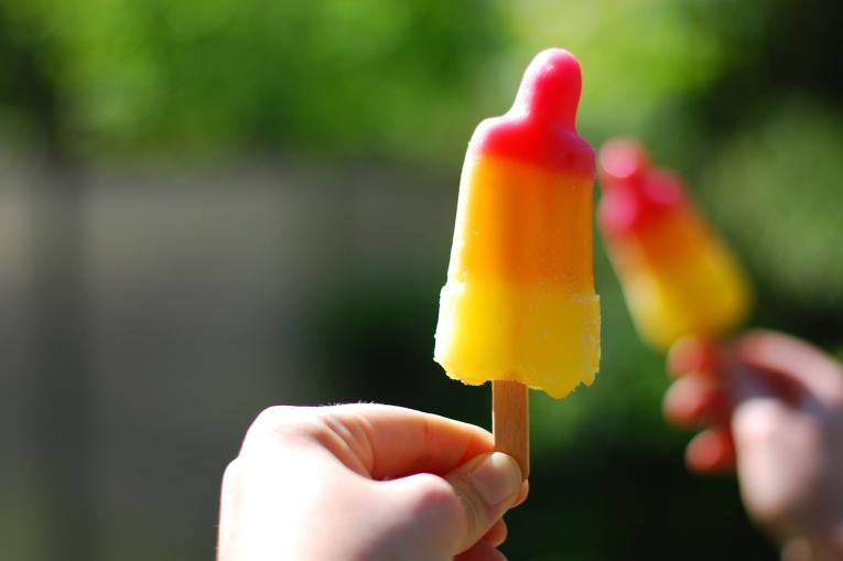 A photo of a rocket ice lolly that is red at the top, orange in the middle and yellow at the bottom. 