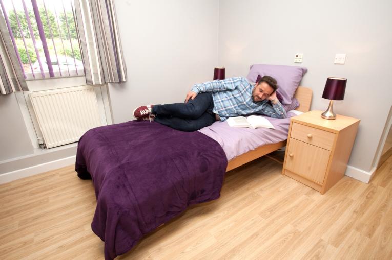 New beginnings - national detox framework - bedroom. A person lying on a single bed with purple sheets. The room is bright with light wooden floors