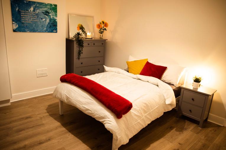 bedroom with a double bed in the centre of the room. There is a bedside table and a chest of drawers next to the bed.