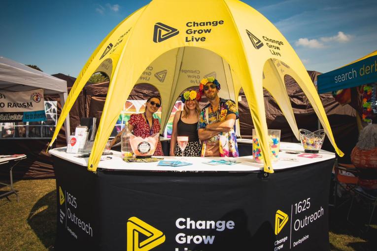 A yellow pop up dome place on top of a round desk. There are three people stood in the middle of the desk.