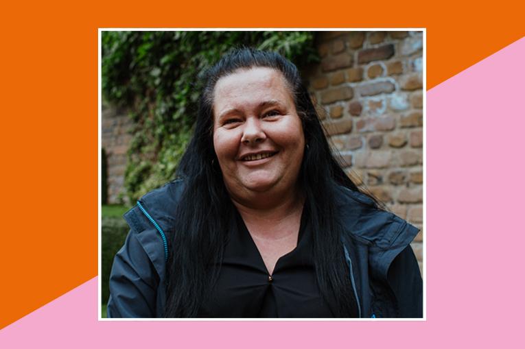 Gemma's photo sits in the centre. She has dark hair and is wearing dark clothes smiling at the camera and stood in front of a brick wall. There is a border around the photo, half orange and half pink.