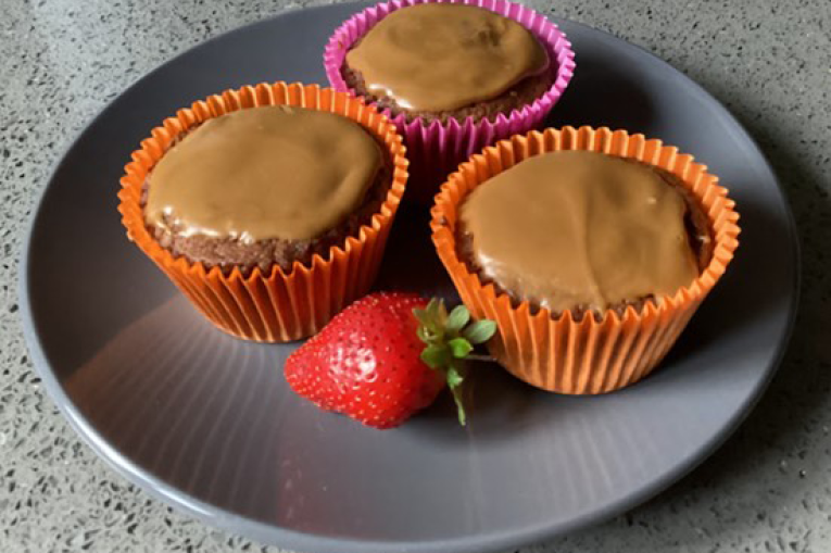 Three biscoff muffins arranged on a grey plate with a strawberry