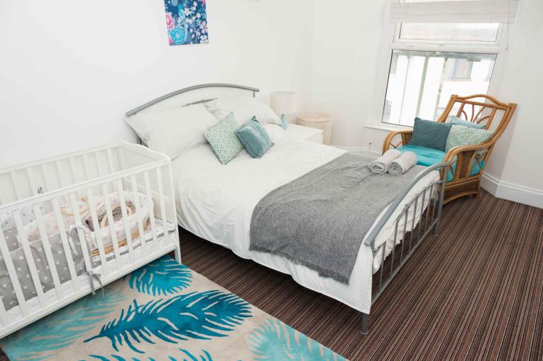 A bedroom with a double bed, a rocking chair and a baby's crib in it