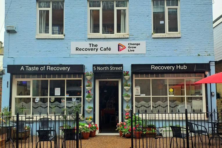 The outside of a blue building with a sign that reads - The Recovery Cafe