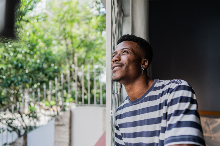 A young man leaning against a doorframe looking out into the garden