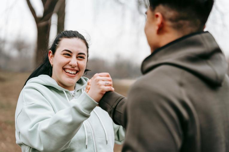 A young woman and a young man outside smiling as they shake hands