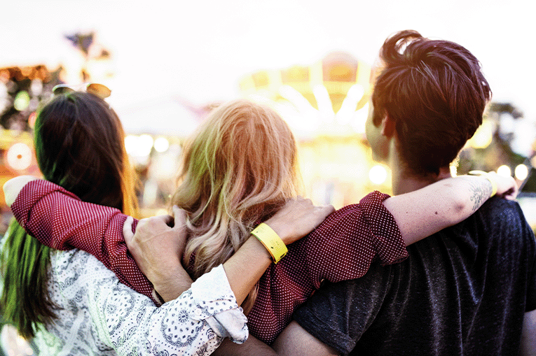 Trio of young people with backs to camera and arms around each other
