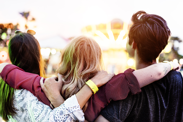 Trio of young people with their backs to the camera with their arms around each other