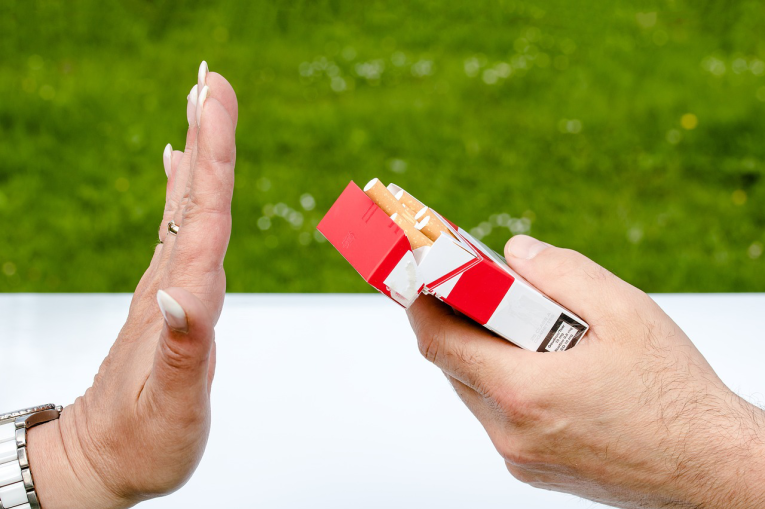 A hand holding a packet offering a packet of cigarettes and another hand saying no