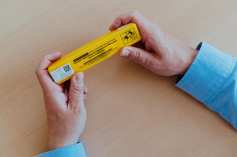 a person's hands holding a bright yellow naloxone kit