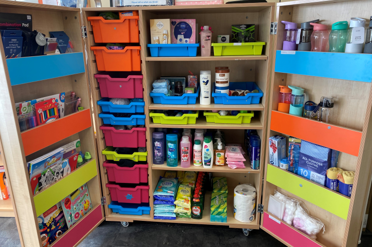 A cupboard with colourful plastic drawers full of essentials such as, toiletries , stationary and cleaning products