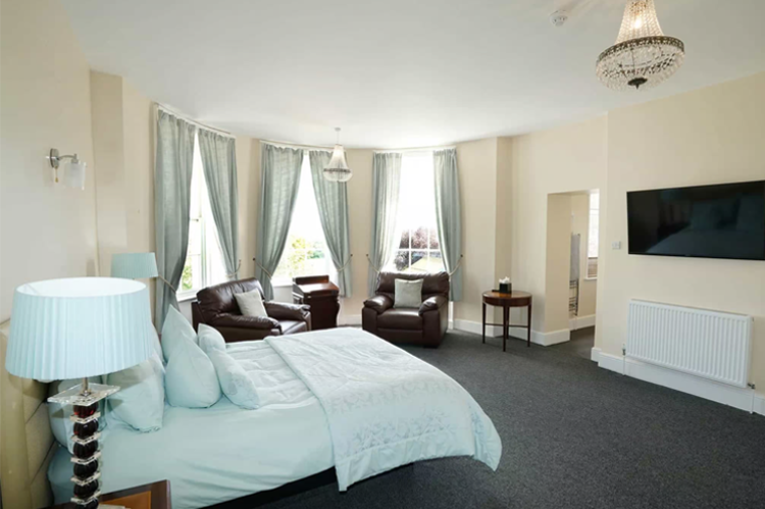 A large, spacious bedroom with a double bed, TV mounted on the wall and floor to ceiling bay windows