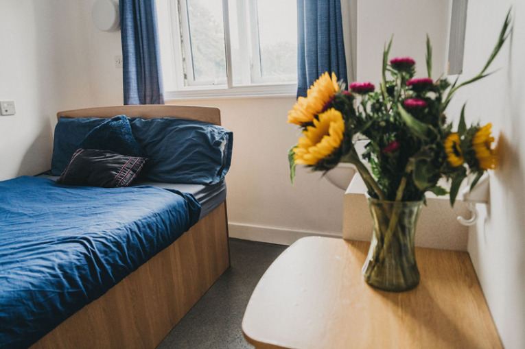 A bedroom with a vase of flowers on the sidetable