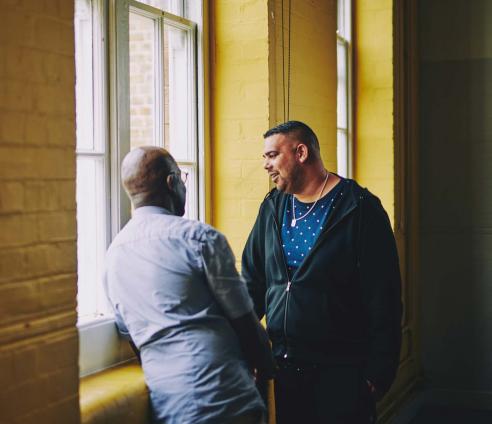 Two men are having a conversation by a window