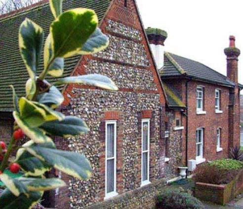 The outside of the building - an old building with brick and stone sections. There is some holly in the foreground.