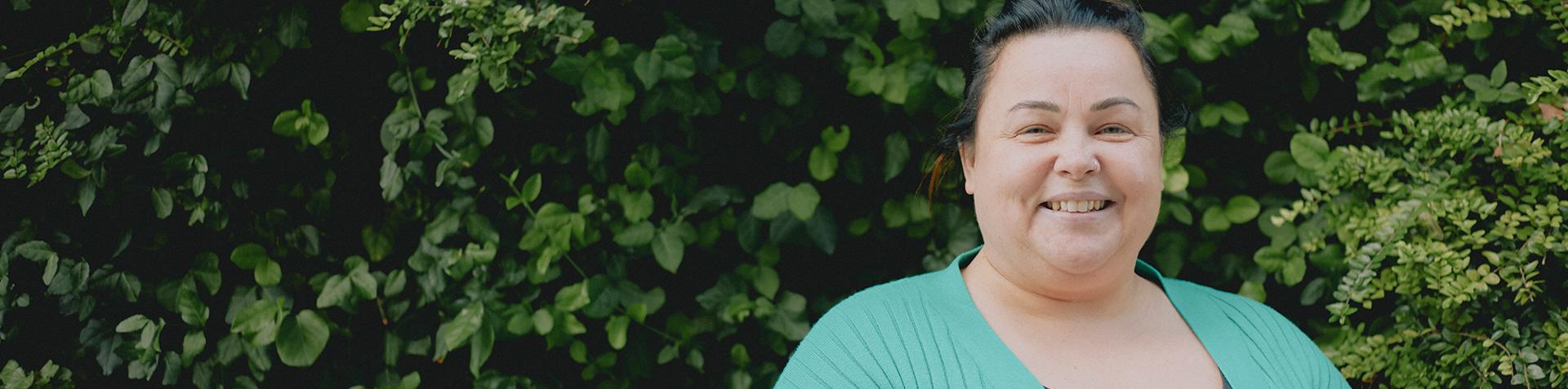 A smiling person looking at the camera with foliage in the background