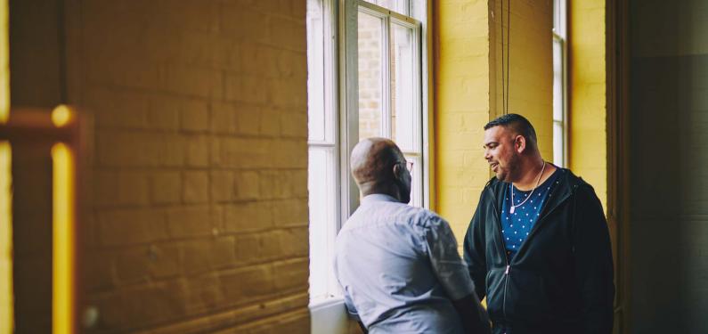 Two men are having a conversation by a window