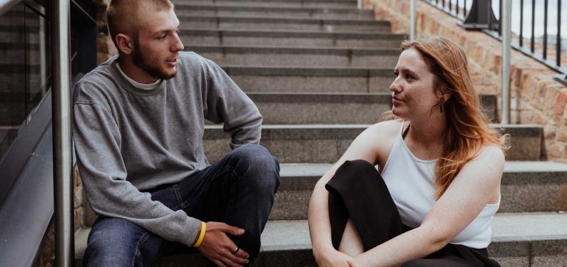 two young people sitting talking to each other on some steps outside