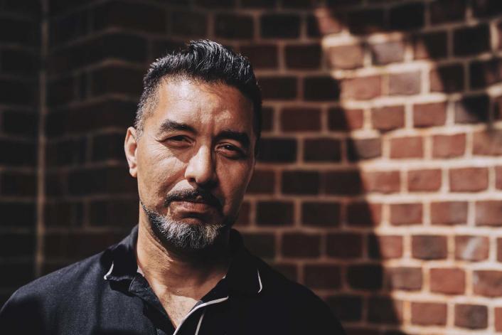 man staring intensely standing in front of a wall with light shining on him