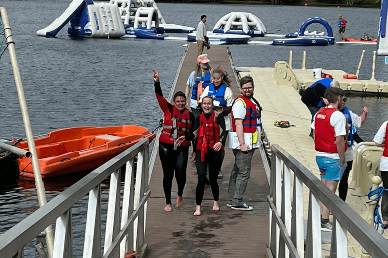 Two women in wetsuits and lifejackets stood in front of an aquapark