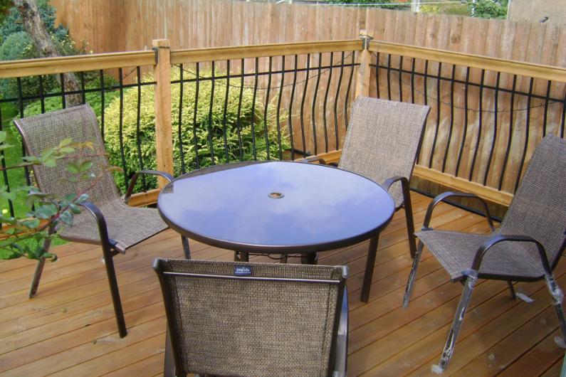 A photo of a table with 4 chairs around it, placed in a garden on top of wooden decking