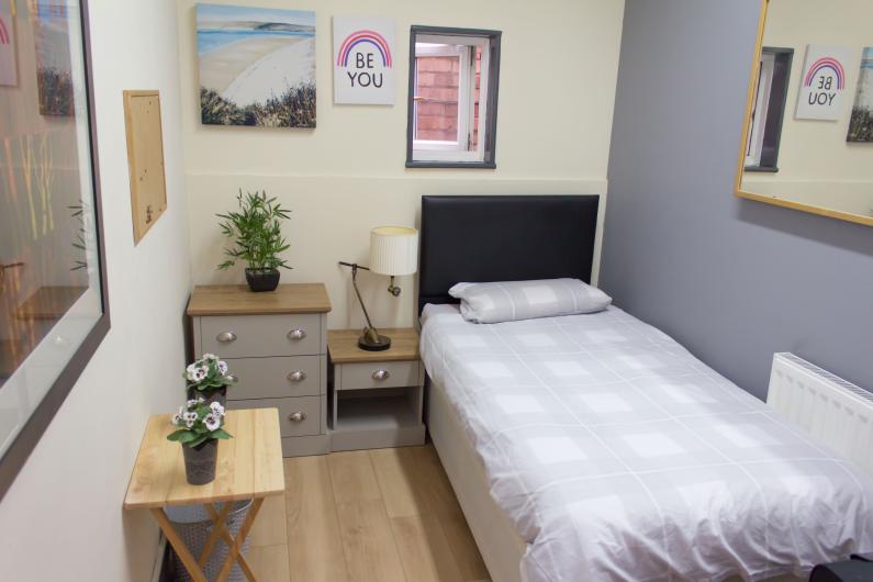 A photo of a bedroom, with a single bed, bed side cabinet, and posters on the walls