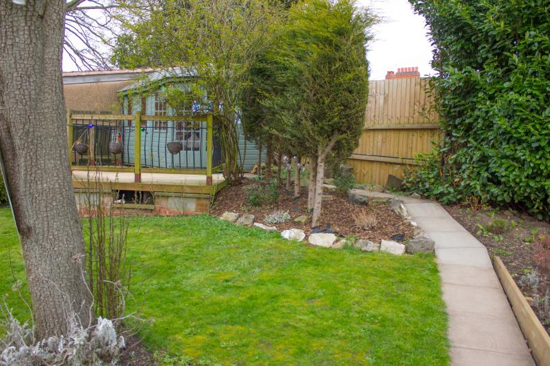  A photo of a garden, with a tree in the foreground on the left hand side, and a path on the right leading down to a shed at the bottom