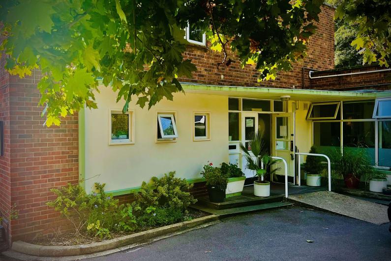 A photo of the outside of the building. There are plenty of windows with a tree over hanging the top of the image.