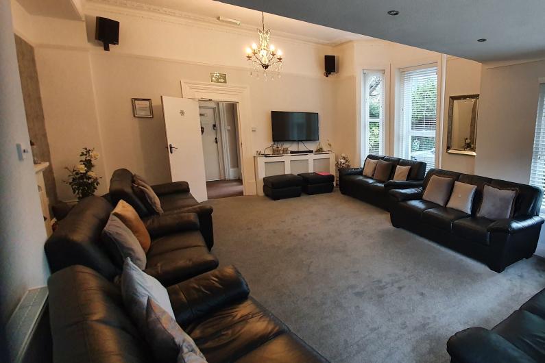 A photo of a communal area. There are four black leather sofa's around the outside of the room and a TV mounted to the back wall.