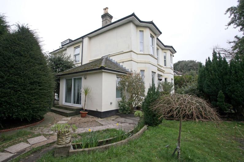 The front of the building of Allington House, it is two floors high. There is a conservatory on the left hand side of the building. It is painted white and there is a garden in front of it. 