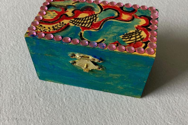A photo of a wooden box that has been painted blue and had pink gems stuck to the lid
