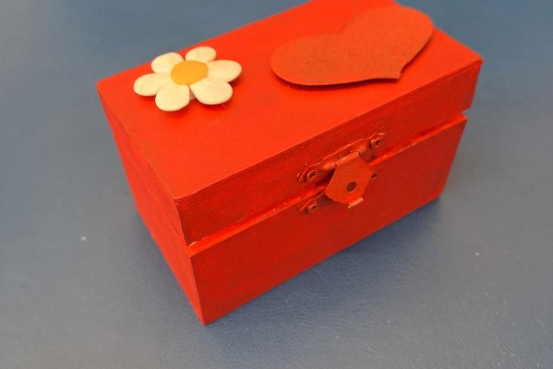 A photo of a wooden box that has been painted orange and had a flower stuck to the lid