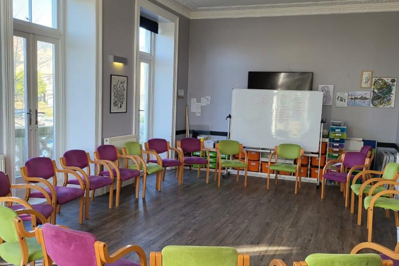 Main group room - a large room with high ceilings. a circle of padded chairs in pink and light green face the centre of the room, and there is a whiteboard on the far wall