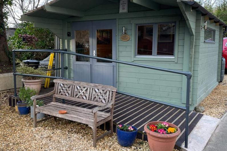 The villa - a large hut painted green. Outside the front is a gravel area with a bench and some large plant pots, and a path runs along the front