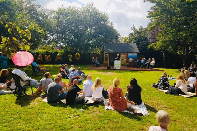 A photo of a garden. There is a big open green space with people sat around chatting. 