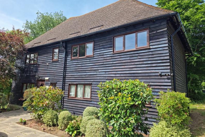 Kenward Trust - a converted barn with dark grey wood. There are hedges in the foreground