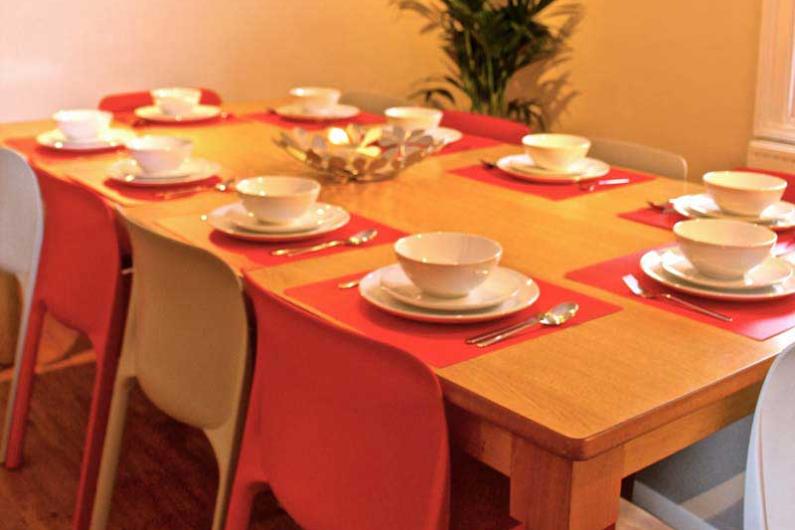 A dining table with orange and beige chairs. The table is laid with white plates and bowls