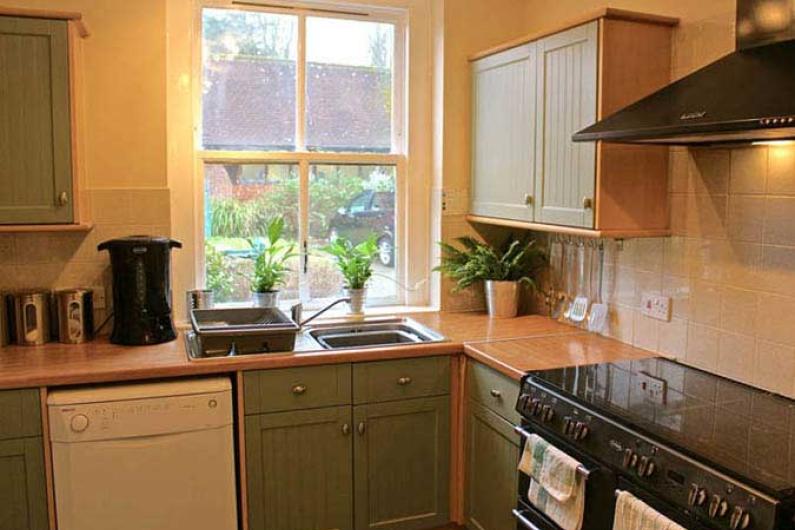 A kitchen with a large sash window, green kitchen cupboards, a dish washer and an oven