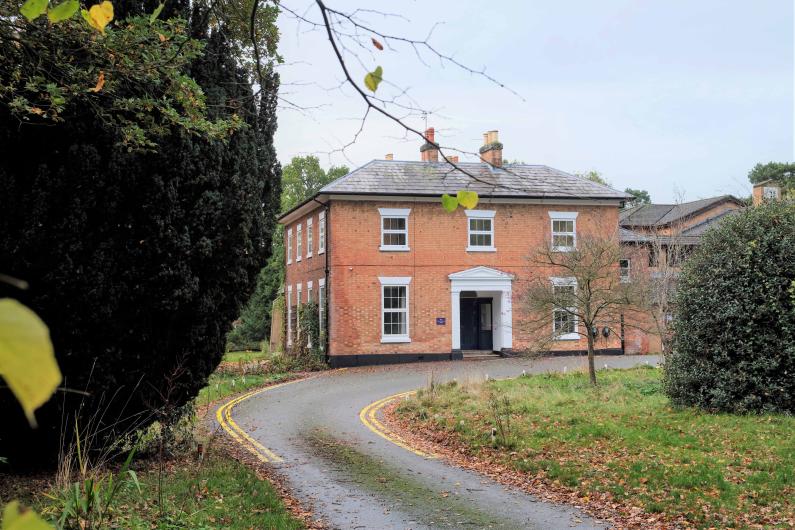 Oakwood from the outside - a large, red-bricked Georgian estate house with a curved drive and hedges in the foreground