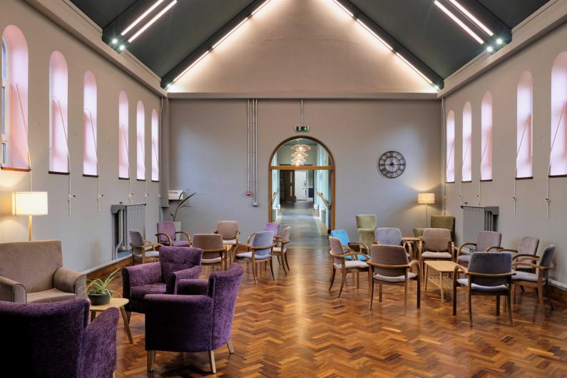 Group space at Oakwood - a large room with vaulted ceilings, wooden floor and lots of windows, there are armchairs and tables throughout the room