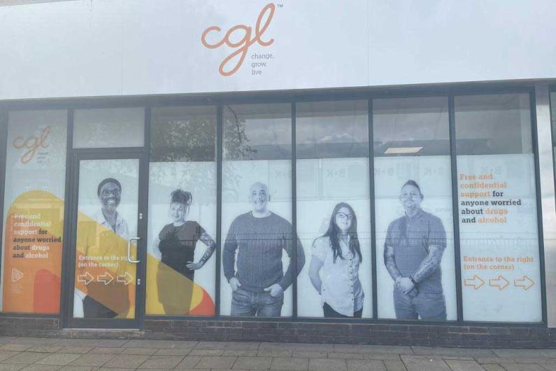 Outside of the Crew building - a white banner says 'CGL' in orange, and the windows have decals of photos of people in them. Each window has a different person