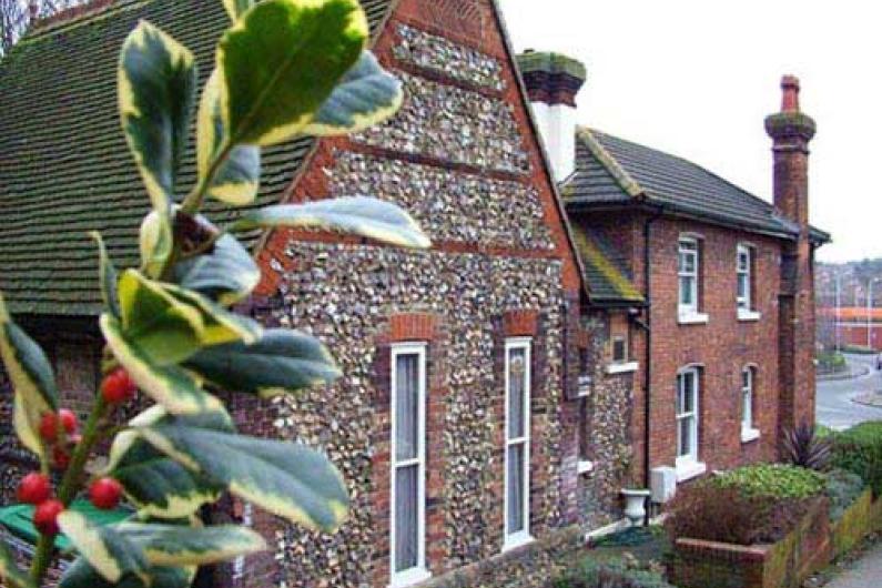 The outside of the building - an old building with brick and stone sections. There is some holly in the foreground.