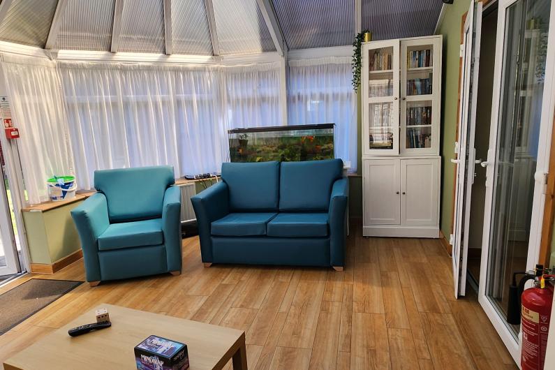 A conservatory. There is wooden floors and lots of windows letting in light. there are three arm chairs around the edge of the room. 