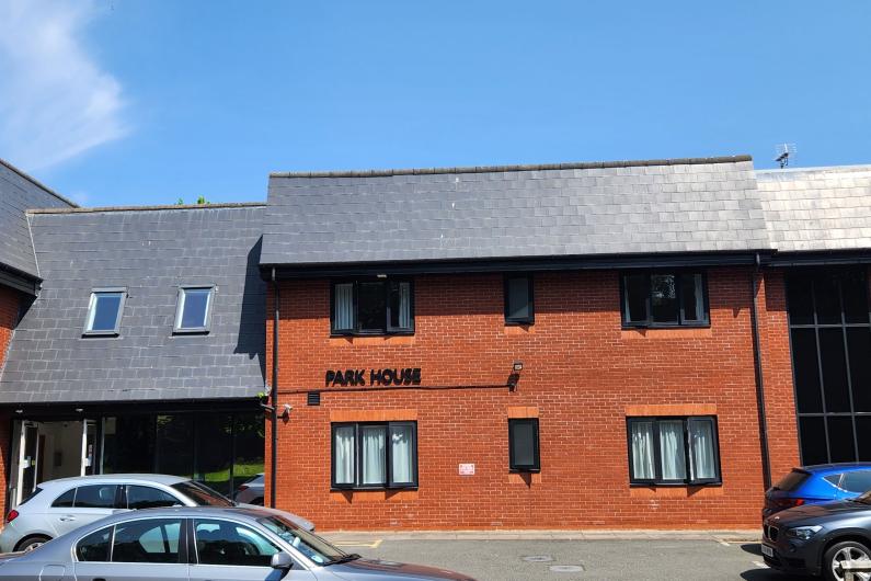 The outside of a modern building. It has red brick walls and a grey slate rood. There are cars parked outside and the words Park House and on the wall of the building