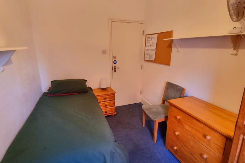 Mount Carmel Bedroom - a green single bed, white walls, blue carpet and pine furniture