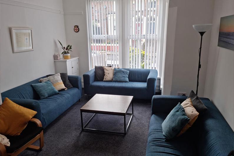 A group room - there are three blue sofas centred around a coffee table, white walls and large windows.